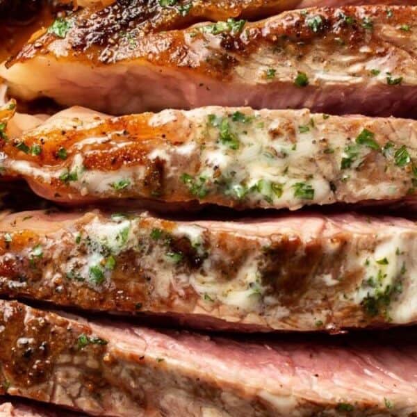 Sliced, cooked steak with a browned crust and juicy pink interior, topped with melted herb butter.