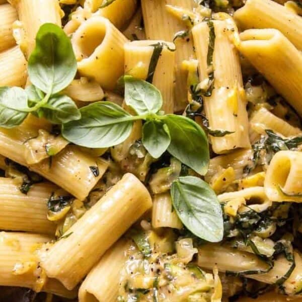 A plate of rigatoni pasta topped with creamy sauce, chopped greens, and fresh basil leaves.