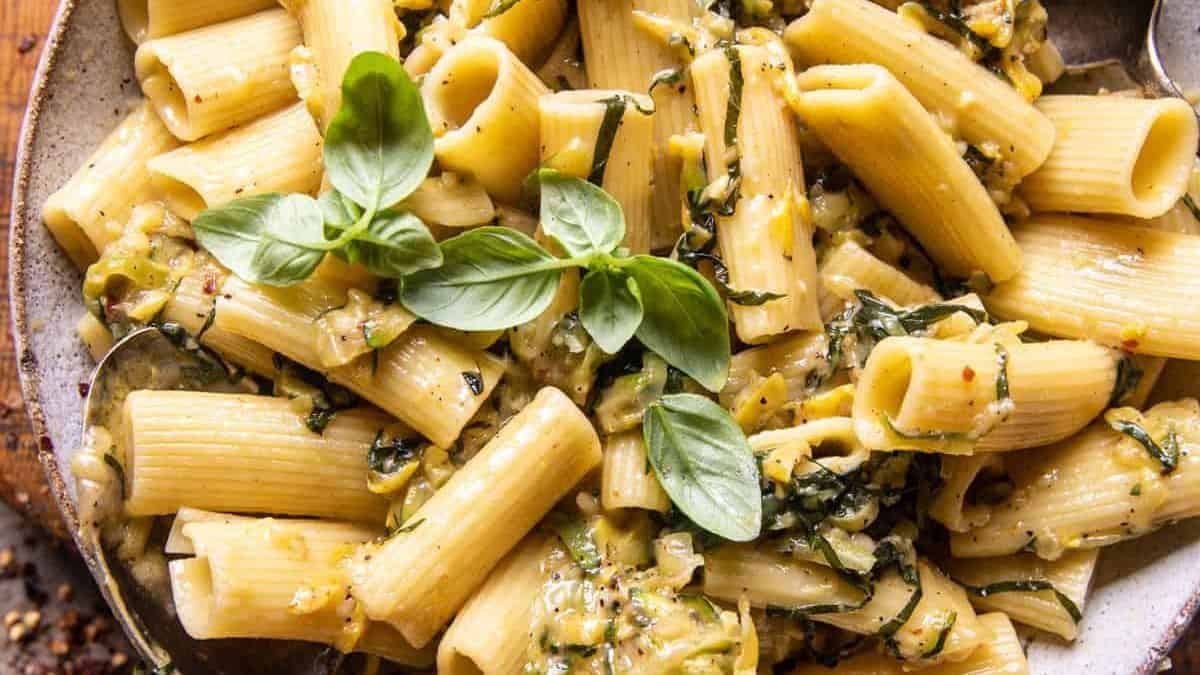 A plate of rigatoni pasta topped with creamy sauce, chopped greens, and fresh basil leaves.