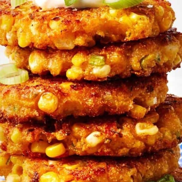A stack of golden brown corn fritters topped with sliced green onions and a dollop of sauce, served on a blue-checkered plate.