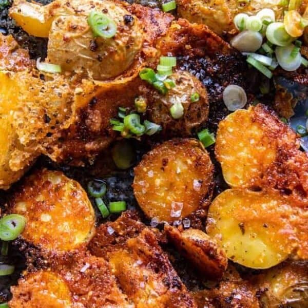 Crispy roasted potato slices topped with melted cheese and sliced green onions on a baking sheet. A metal spatula rests nearby.