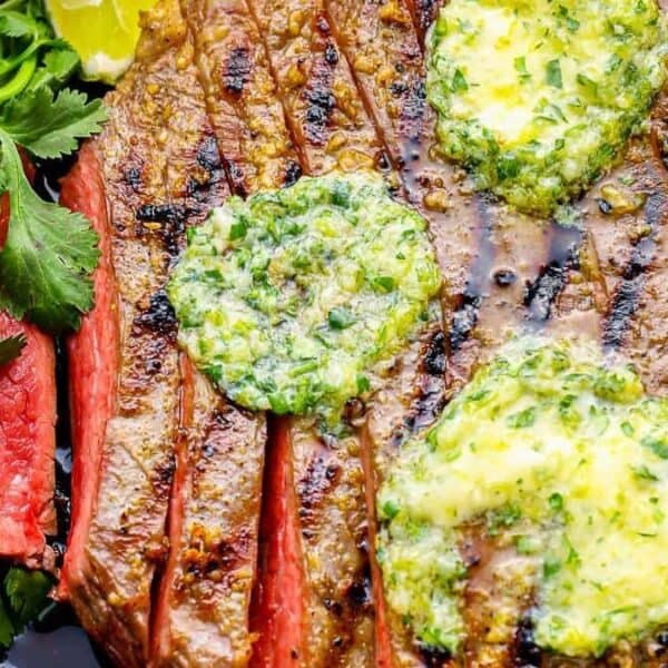 A grilled steak with a dollop of herb butter on top, accompanied by fresh cilantro and a lemon wedge.
