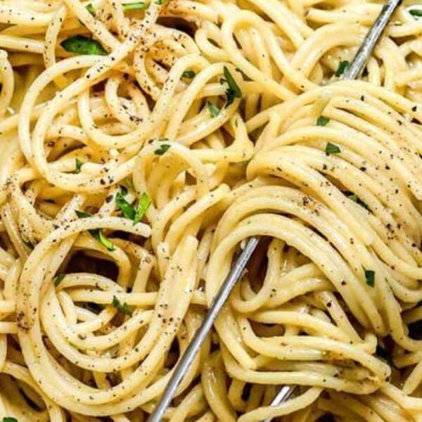 A plate of spaghetti coated in a creamy sauce, topped with black pepper and herbs, with a fork twisting some of the noodles.