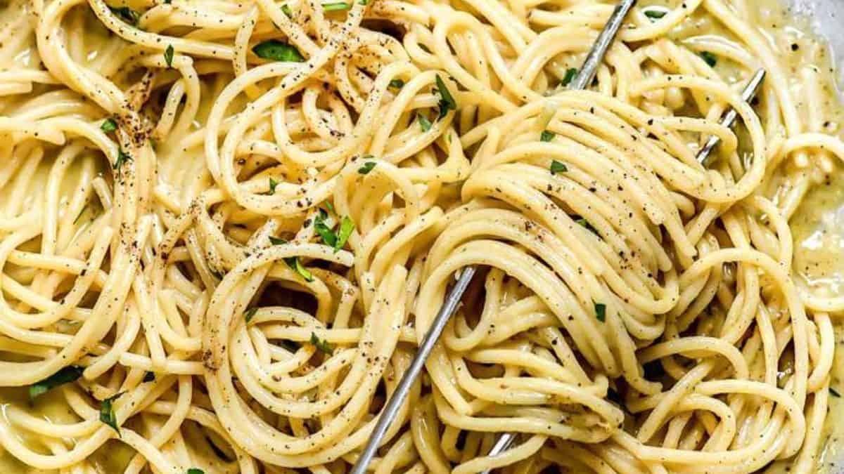 A plate of spaghetti coated in a creamy sauce, topped with black pepper and herbs, with a fork twisting some of the noodles.