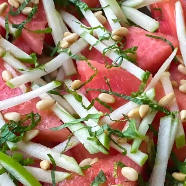 Slices of watermelon with julienned cucumber, fresh herbs, and pine nuts on top.