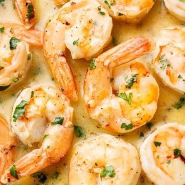 Cooked shrimp in a creamy garlic sauce, garnished with chopped herbs and sliced lemon.