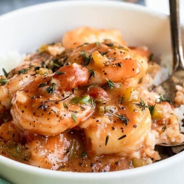 A bowl filled with shrimp étouffée over white rice, topped with chopped herbs, and a spoon resting inside the bowl.