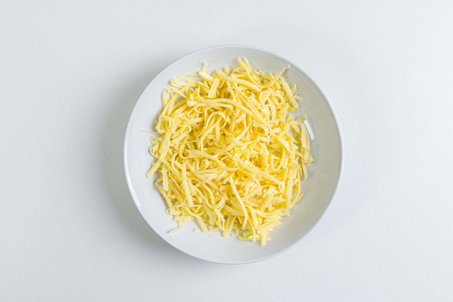 A white plate containing shredded yellow cheese on a white surface.
