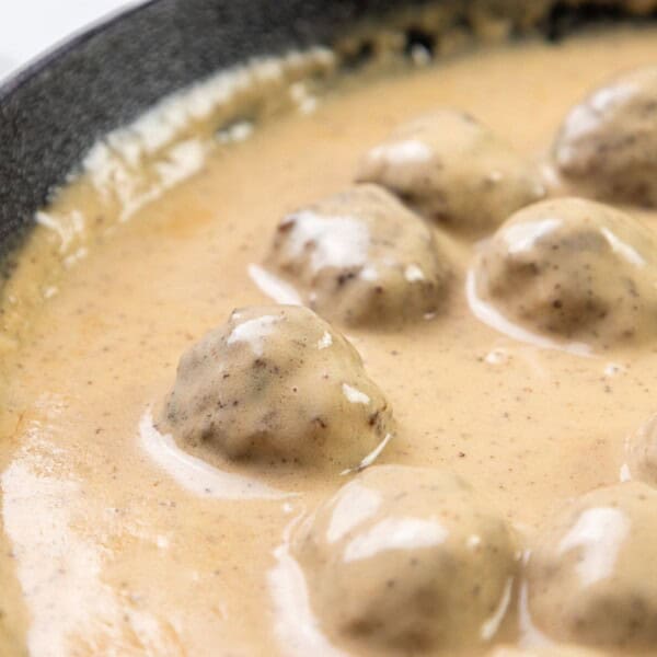 Meatballs resting in a creamy beige sauce inside a black skillet.