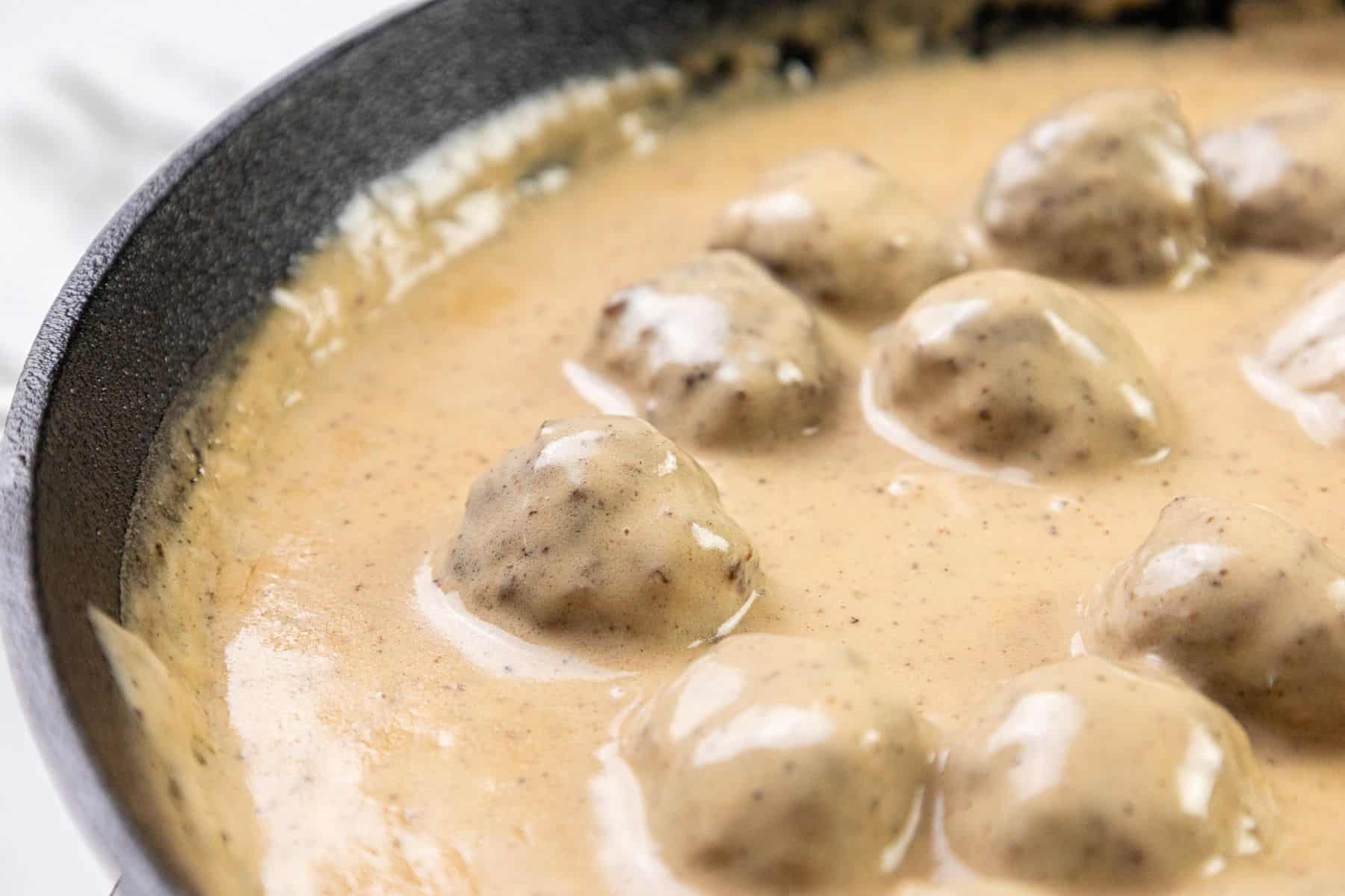 Meatballs resting in a creamy beige sauce inside a black skillet.