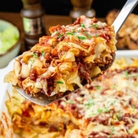 A serving spoon with baked pasta, tomato sauce, ground meat, melted cheese, and herbs.