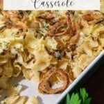 A rectangular dish filled with French onion noodle casserole, topped with crispy fried onions and garnished with chopped parsley.
