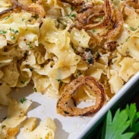 Cooked egg noodles mixed with herbs and topped with crispy fried onions, served in a white dish.