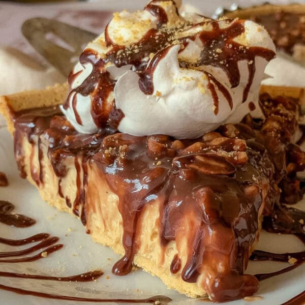 A slice of pie with whipped cream and chocolate drizzle on a white plate; a fork is placed next to it.