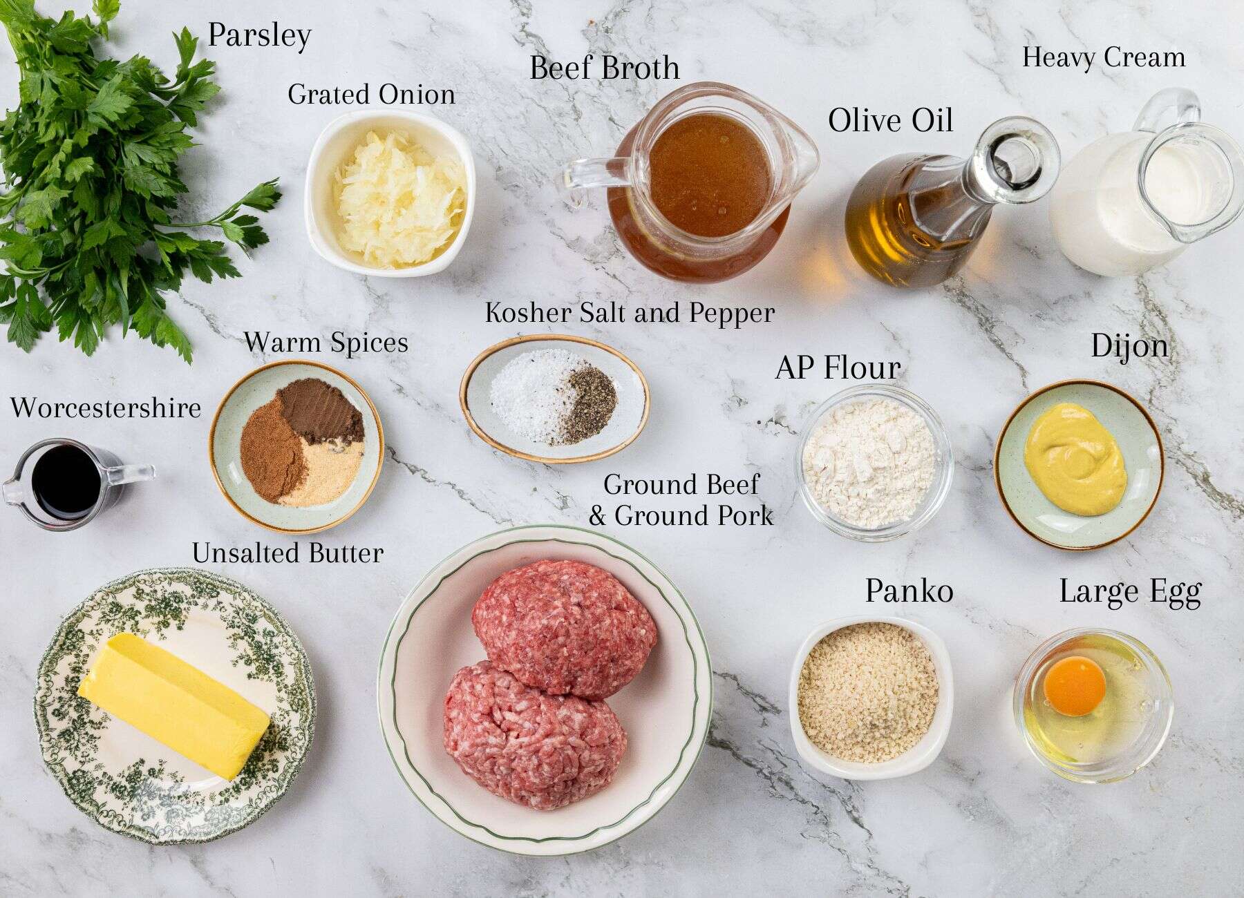Ground beef and pork, egg, assorted spices, flour, panko breadcrumbs, onion, butter, broth, parsley, olive oil, cream, and Dijon mustard arranged on a marble countertop.