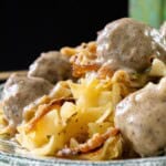 Egg noodles topped with creamy meatballs and crispy onions, served on a patterned plate.