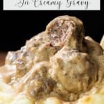 A plate with several meatballs covered in creamy gravy, served on a bed of mashed potatoes; one meatball is cut open, revealing its interior.