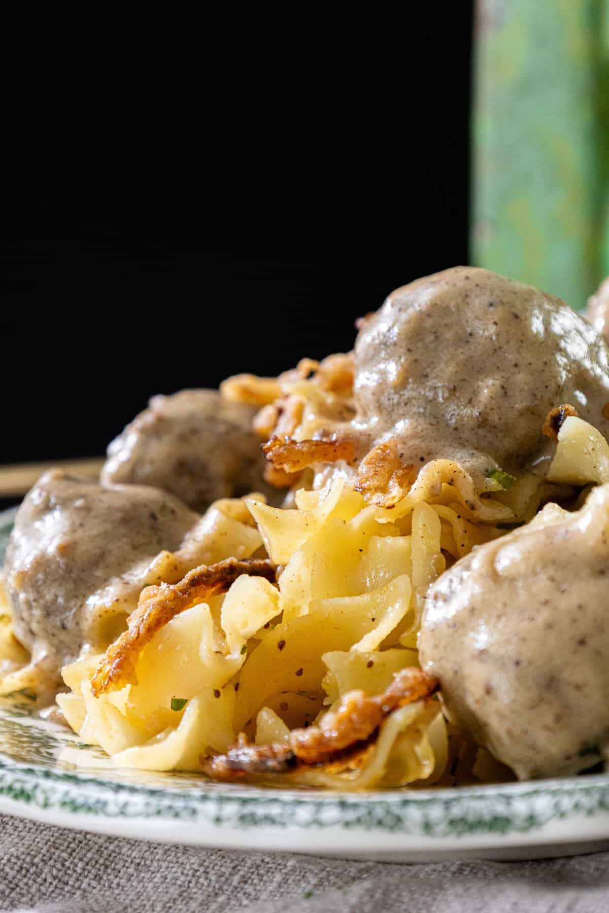 A patterned plate holding pasta noodles, meatballs, creamy sauce, and caramelized onions.