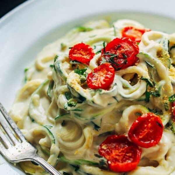 A plate of creamy pasta garnished with halved cherry tomatoes and fresh herbs, with a fork placed on the plate's edge.