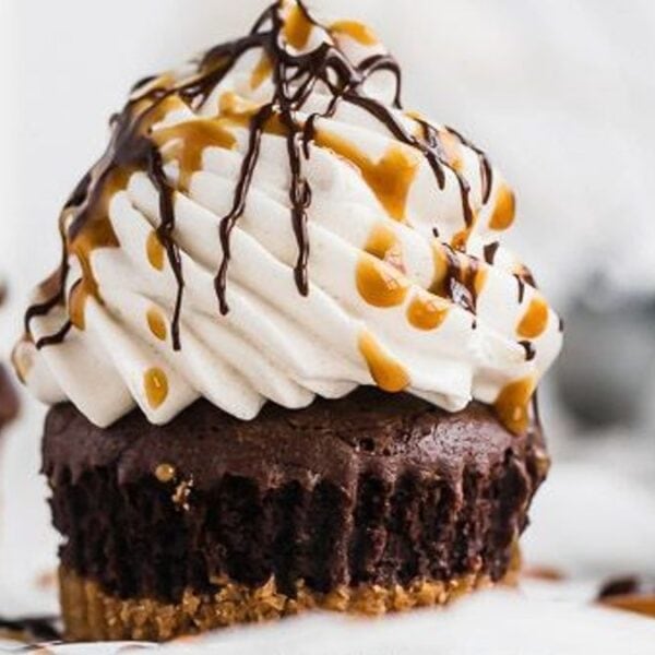 A chocolate cupcake with a crumbly base, swirled whipped cream on top, and drizzles of chocolate and caramel sauce.
