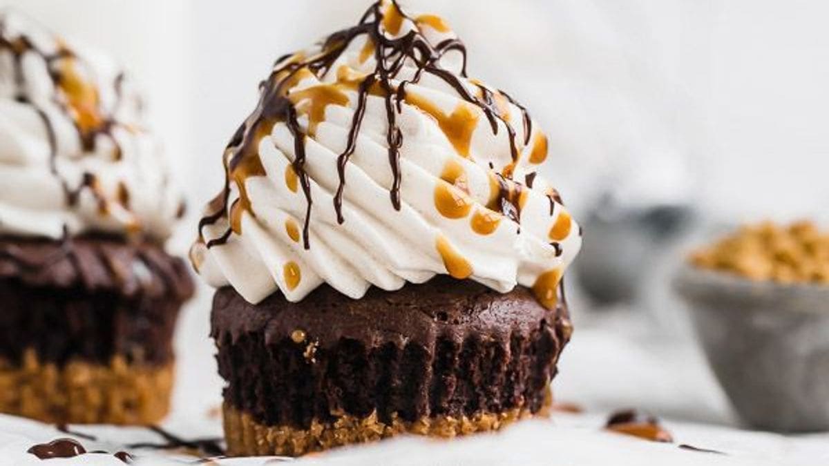 A chocolate cupcake with a crumbly base, swirled whipped cream on top, and drizzles of chocolate and caramel sauce.