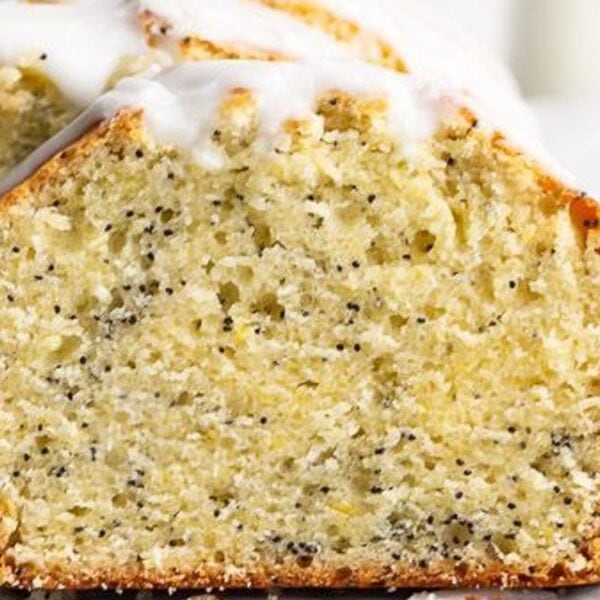 Slices of lemon poppy seed loaf cake with white icing on top are arranged on a white surface next to a knife.