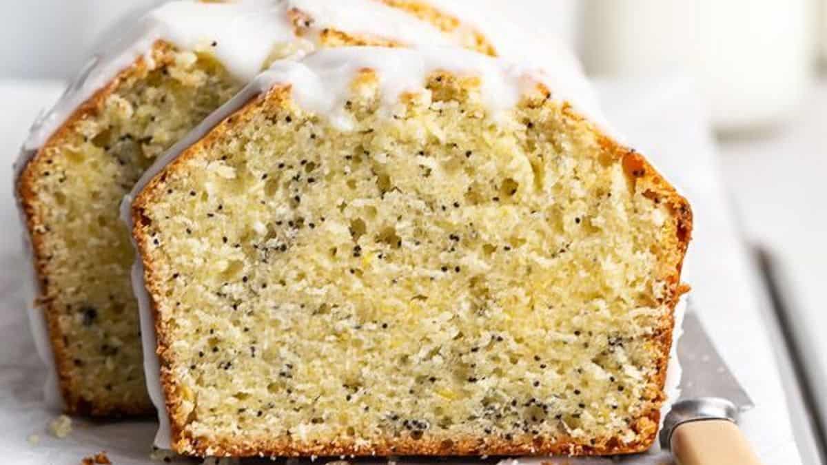 Slices of lemon poppy seed loaf cake with white icing on top are arranged on a white surface next to a knife.