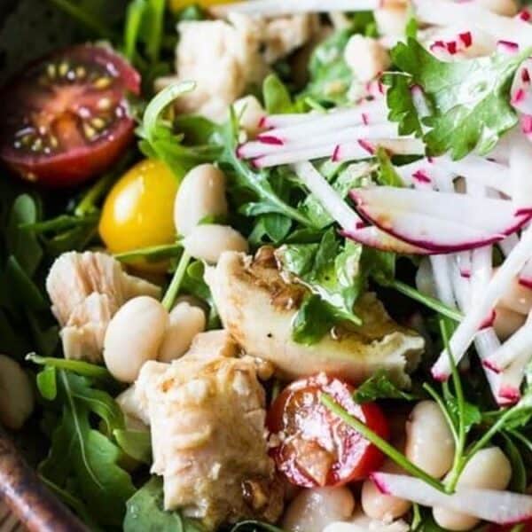 A bowl containing mixed greens, cherry tomatoes, white beans, grilled chicken slices, sliced radishes, and cilantro.