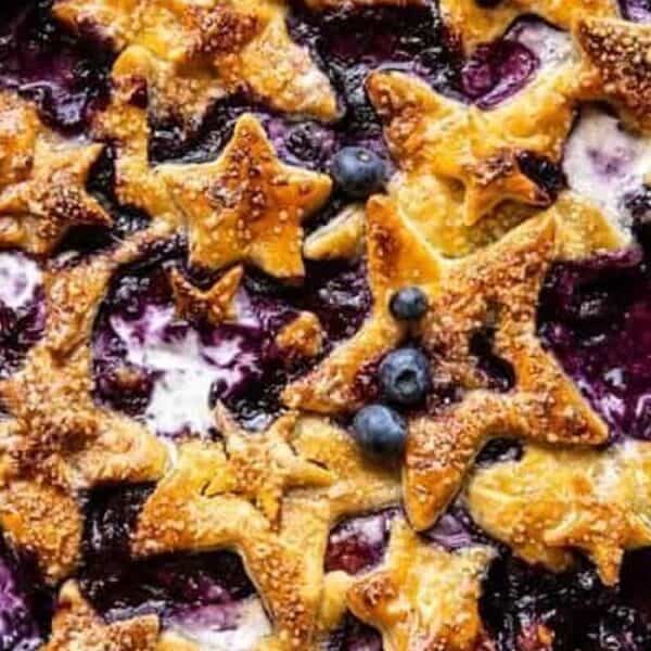 A pan filled with a baked blueberry mixture, topped with golden, star-shaped pastry pieces and scattered whole blueberries.