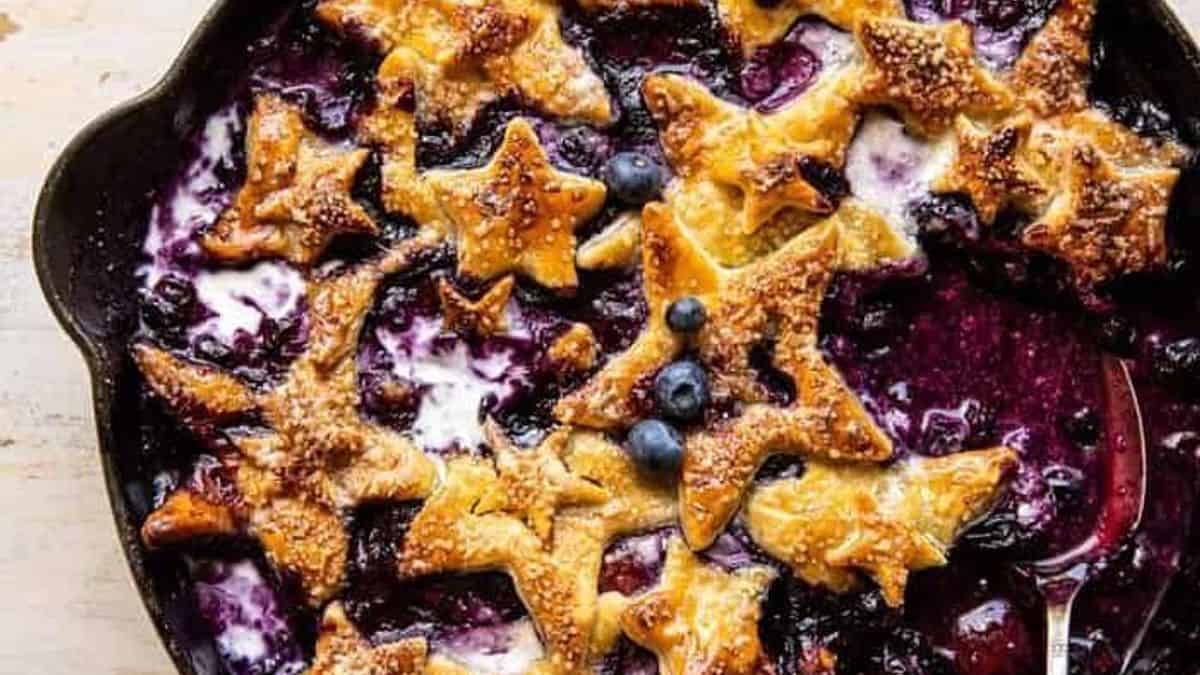 A pan filled with a baked blueberry mixture, topped with golden, star-shaped pastry pieces and scattered whole blueberries.