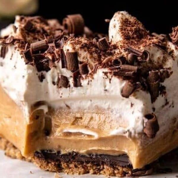A slice of dessert with a crumbly crust, creamy filling, a layer of whipped topping, and chocolate shavings on top.