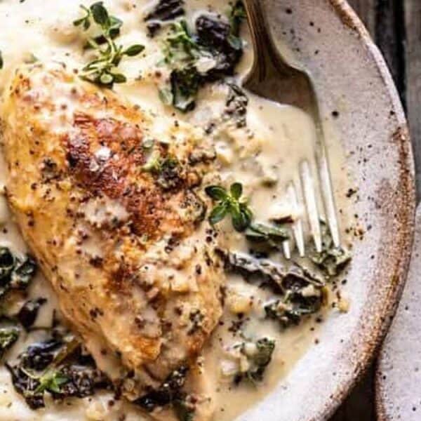 A plate with sliced cooked chicken breast, creamy sauce, wilted greens, and a sprinkle of fresh herbs on top.