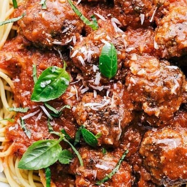 A plate of spaghetti with tomato sauce, meatballs, grated cheese, and fresh basil leaves.