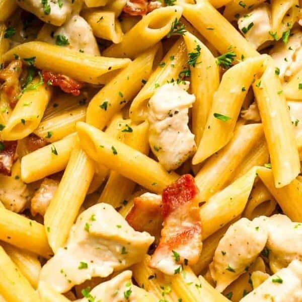 Close-up of penne pasta with pieces of chicken, bacon, and chopped parsley.