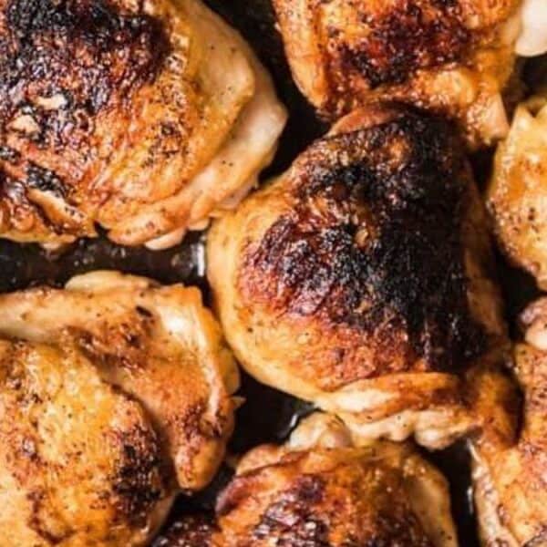 Seven browned chicken thighs in a black skillet.