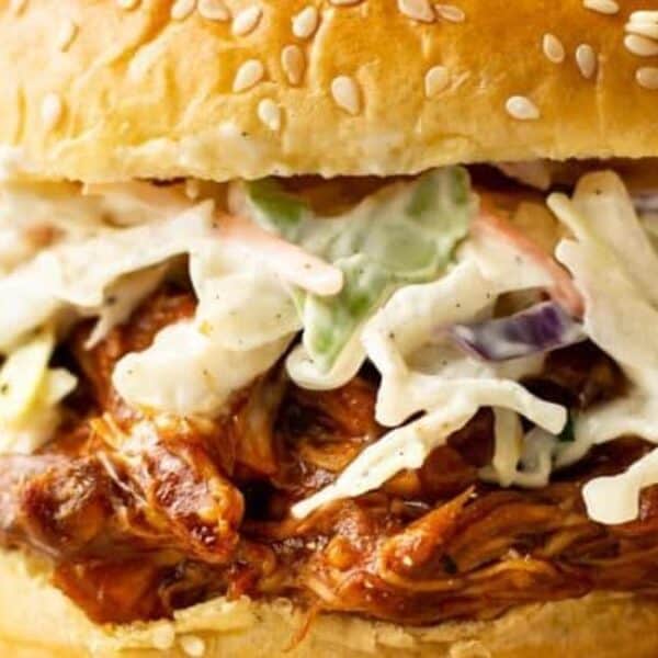 A sesame seed bun sandwich filled with shredded barbecue meat and creamy coleslaw.