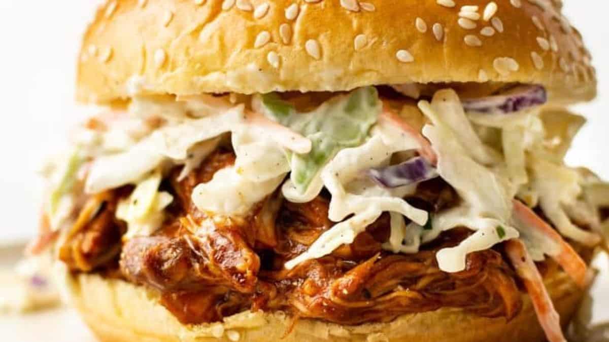 A sesame seed bun sandwich filled with shredded barbecue meat and creamy coleslaw.