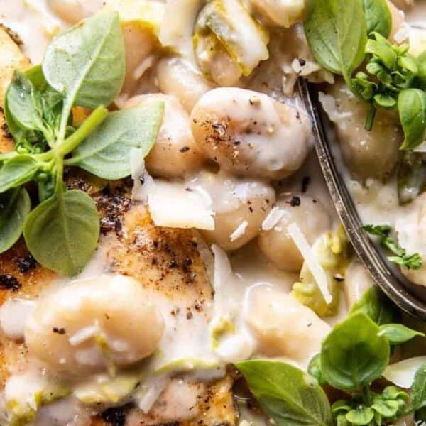 A grilled chicken breast sits atop a creamy white bean sauce, garnished with fresh basil leaves. A fork rests on the plate.