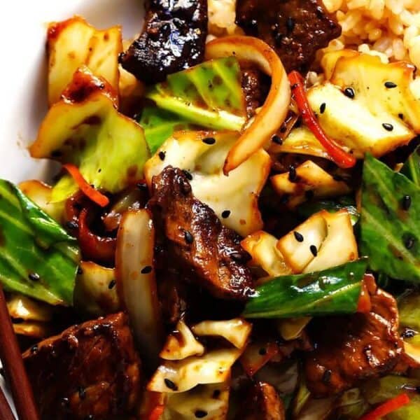 A plate with stir-fried beef, cabbage, onions, and bell peppers alongside a serving of brown rice; chopsticks are placed beside the plate.
