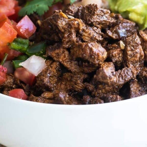 A white bowl containing seasoned steak, diced tomatoes, cilantro-lime rice, pinto beans, and guacamole.