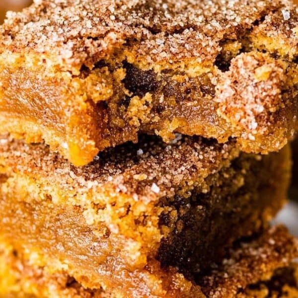 Two stacked cookie bars coated in cinnamon-sugar, with a gooey caramel center, resting on a white surface.