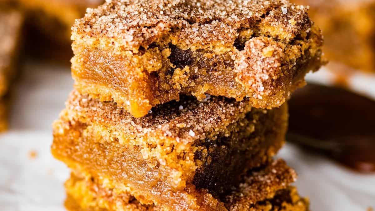 Two stacked cookie bars coated in cinnamon-sugar, with a gooey caramel center, resting on a white surface.