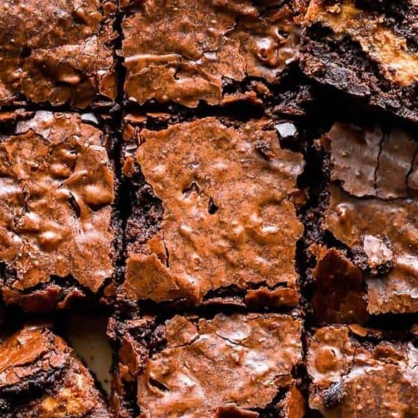 Nine square chocolate brownies with cracked, shiny tops are arranged on parchment paper.