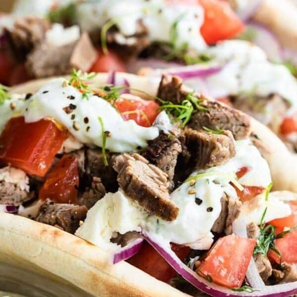 A pita bread filled with sliced grilled meat, diced tomatoes, red onion, fresh herbs, and a white yogurt-based sauce.