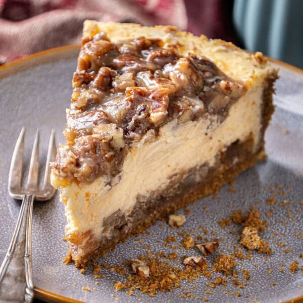 A slice of cheesecake with chopped nuts on top, a gray plate, a fork, and scattered crumbs.