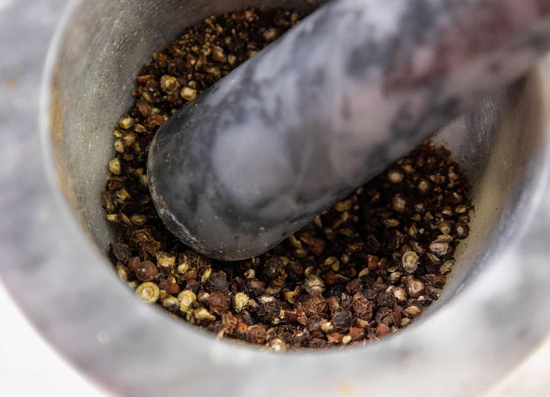 Crushed black peppercorns, a pestle, and a mortar.