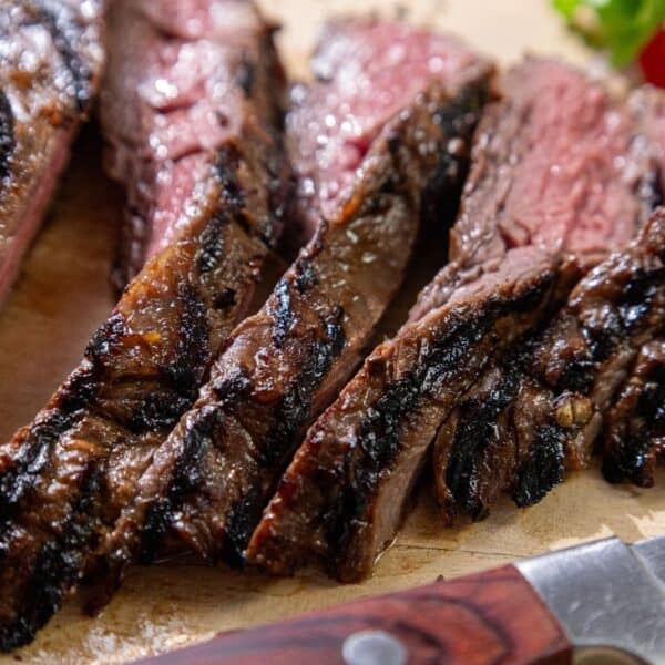 Sliced steak with a charred exterior and pink interior on a cutting board, knife placed beside it.