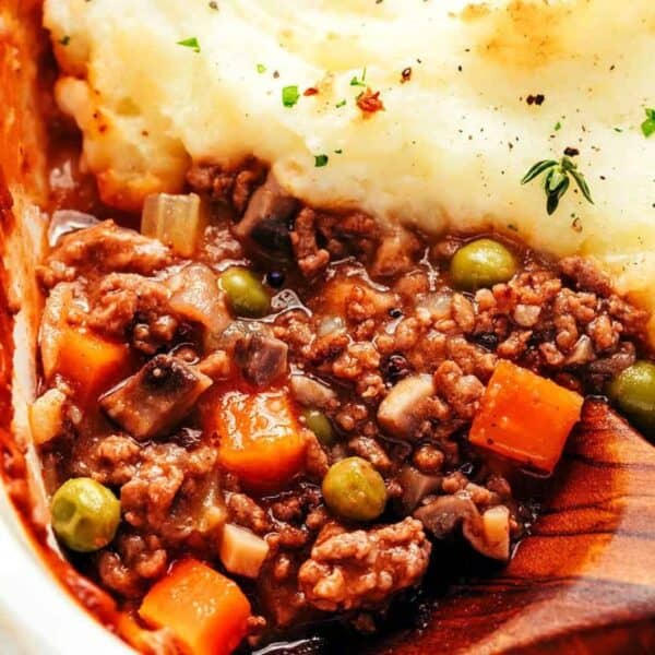 Ground meat, carrots, peas, and gravy topped with mashed potatoes in a baking dish; wooden spoon.
