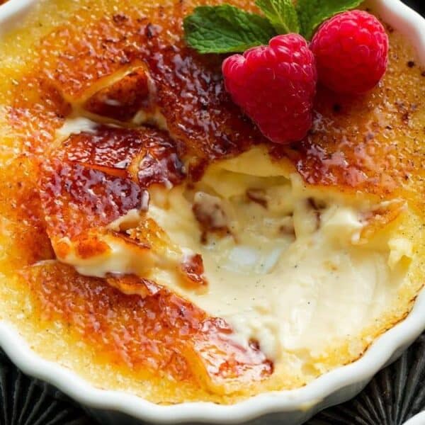 Crème brûlée in a dish with caramelized sugar crust, cracked open to show custard, topped with raspberries and mint leaves.