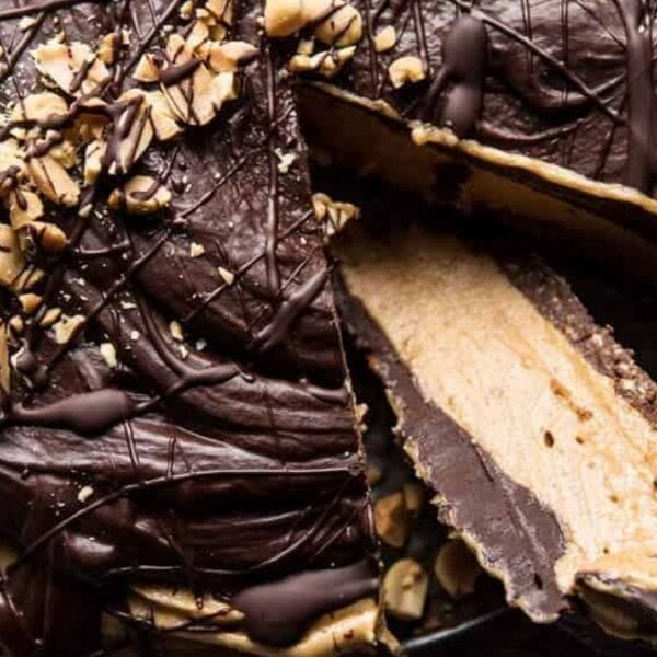 A chocolate peanut butter pie with a slice removed, revealing layers, topped with chopped peanuts and drizzled chocolate.